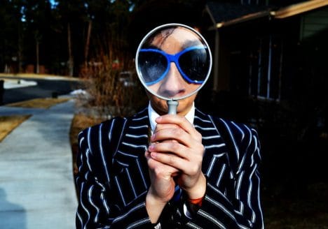 person using magnifying glass enlarging the appearance of his nose and sunglasses